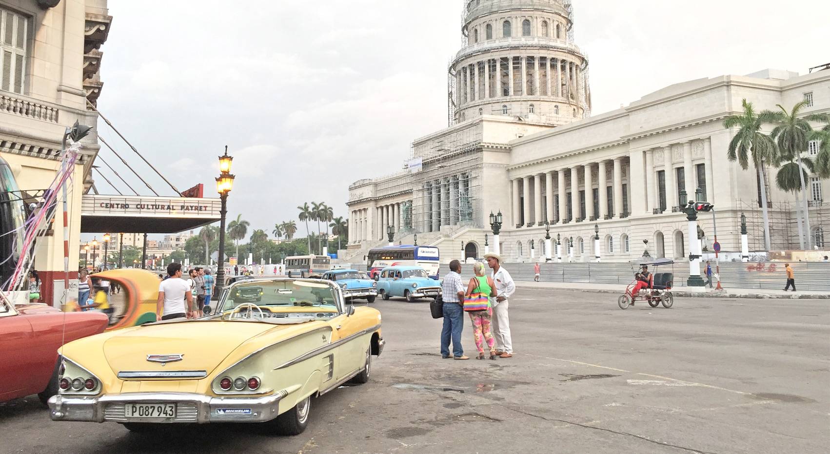 A yellow classic American car in front of the Capitolio in Havana